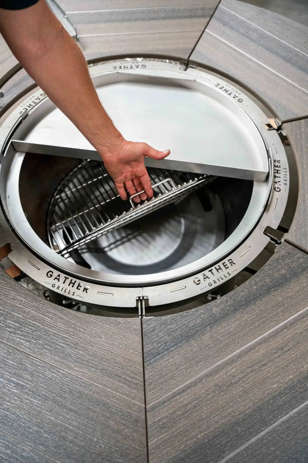 Hand lifting cooking grate on round multi-functional charcoal grill with wood table surface