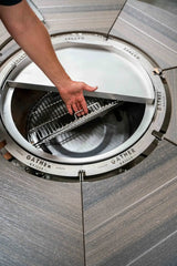 Hand lifting cooking grate on round multi-functional charcoal grill with wood table surface