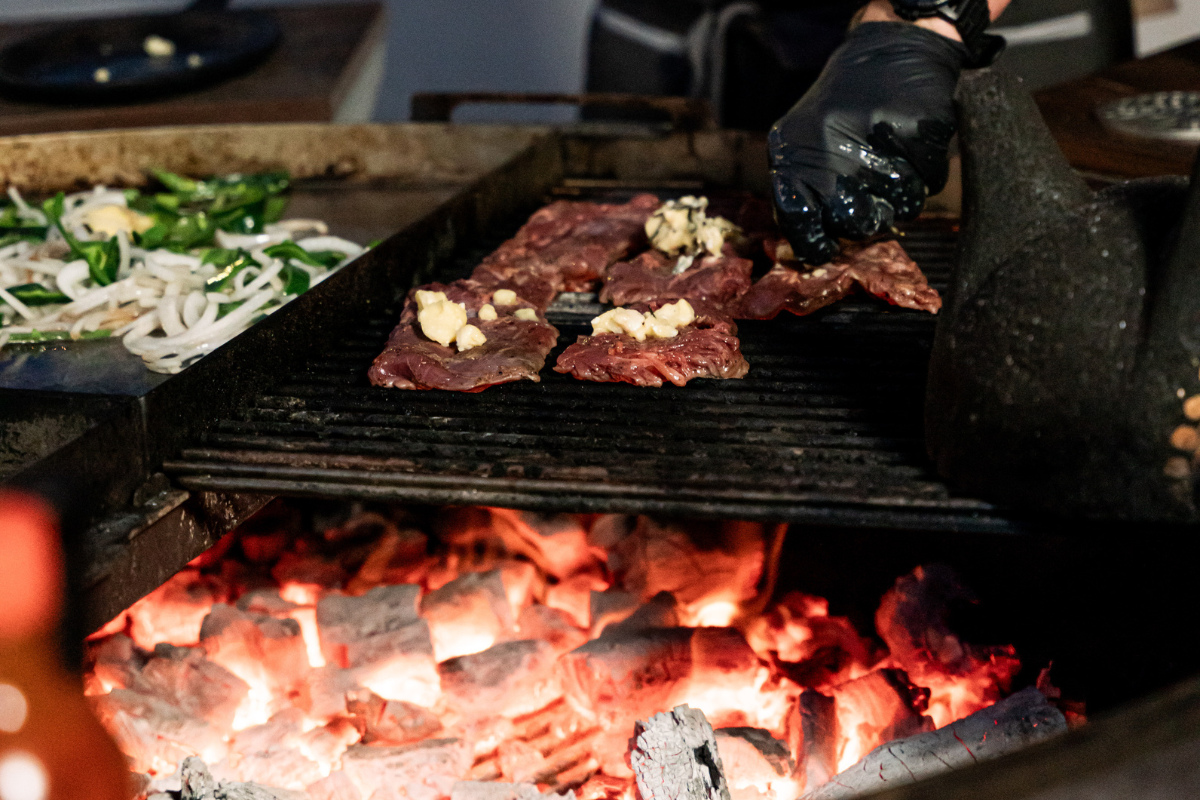 Charcoal grill with sizzling steak, melting butter, onions, peppers, and glowing embers