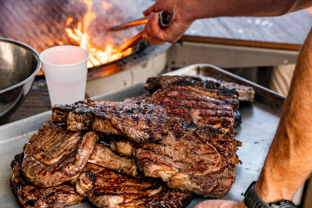 Juicy grilled steaks resting on a tray near a charcoal grill with open flames