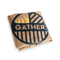 Folded grill cover with 'GATHER' logo, flame graphic, and brown fabric on black background