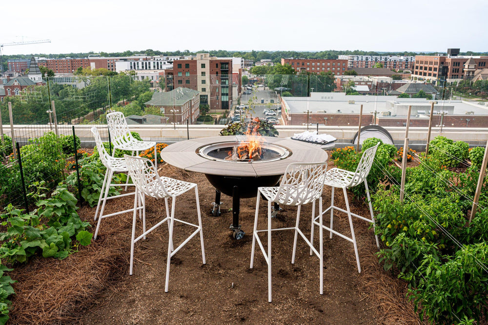 Modern rooftop patio with rotating charcoal grill, fire pit, bar stools, and city view