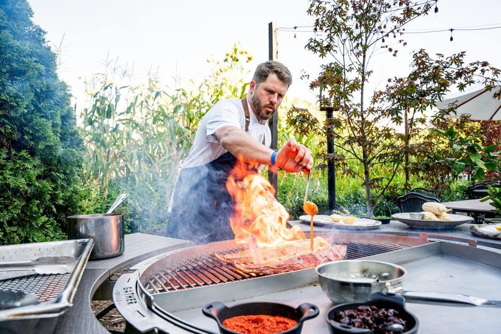Chef grilling meat over open flame on a multi-functional charcoal grill in a garden setting