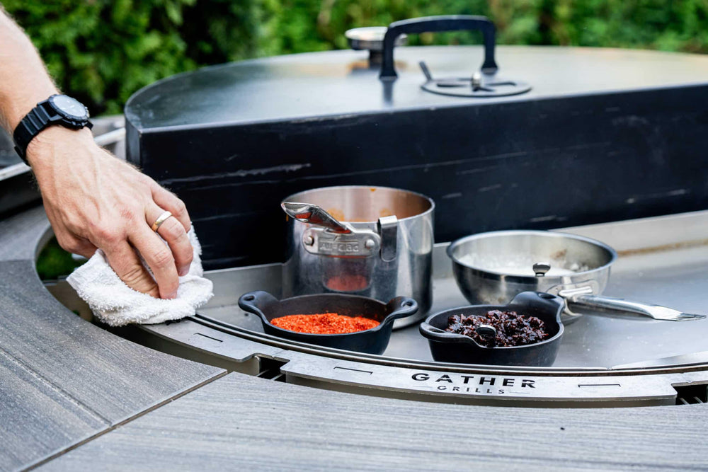 Hand cleaning a multi-functional charcoal grill with spices and utensils on the grill surface outdoors