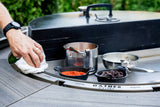 Hand cleaning a multi-functional charcoal grill with spices and utensils on the grill surface outdoors